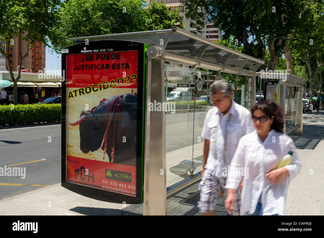 A couple pass by an anti bullfighting poster on a bus stop in Benidorm, Spain. Stock Photo