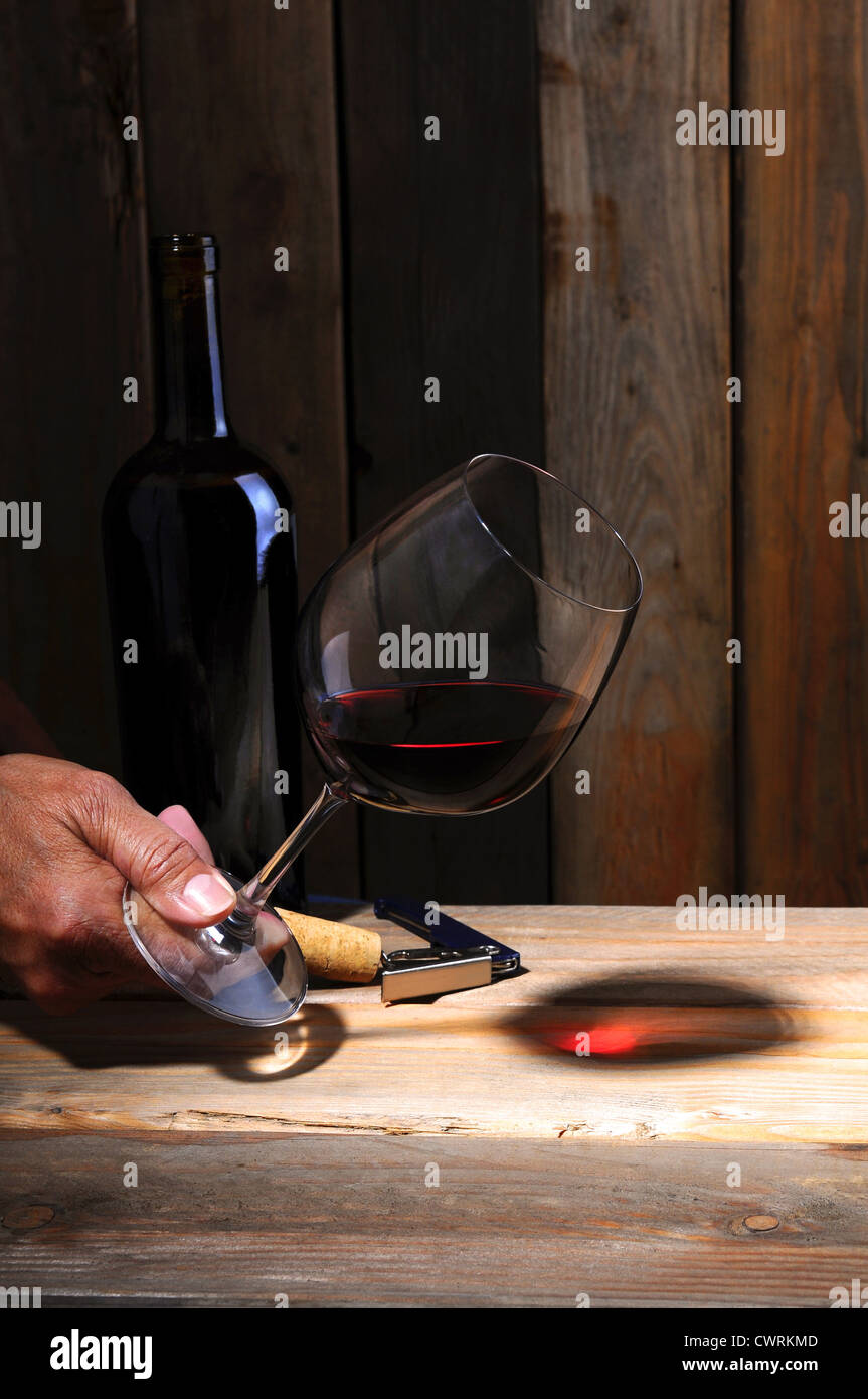 A winemaker holding a glass of wine to study its color in a wine cellar setting. Closeup on hand glass and bottle only. Stock Photo