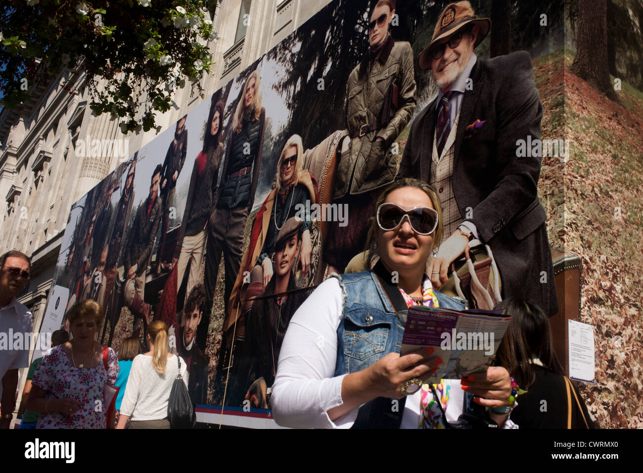 Woman passes below a billboard for clothing retailer Tommy Hilfiger showing the wealthy classes in a country setting. Stock Photo