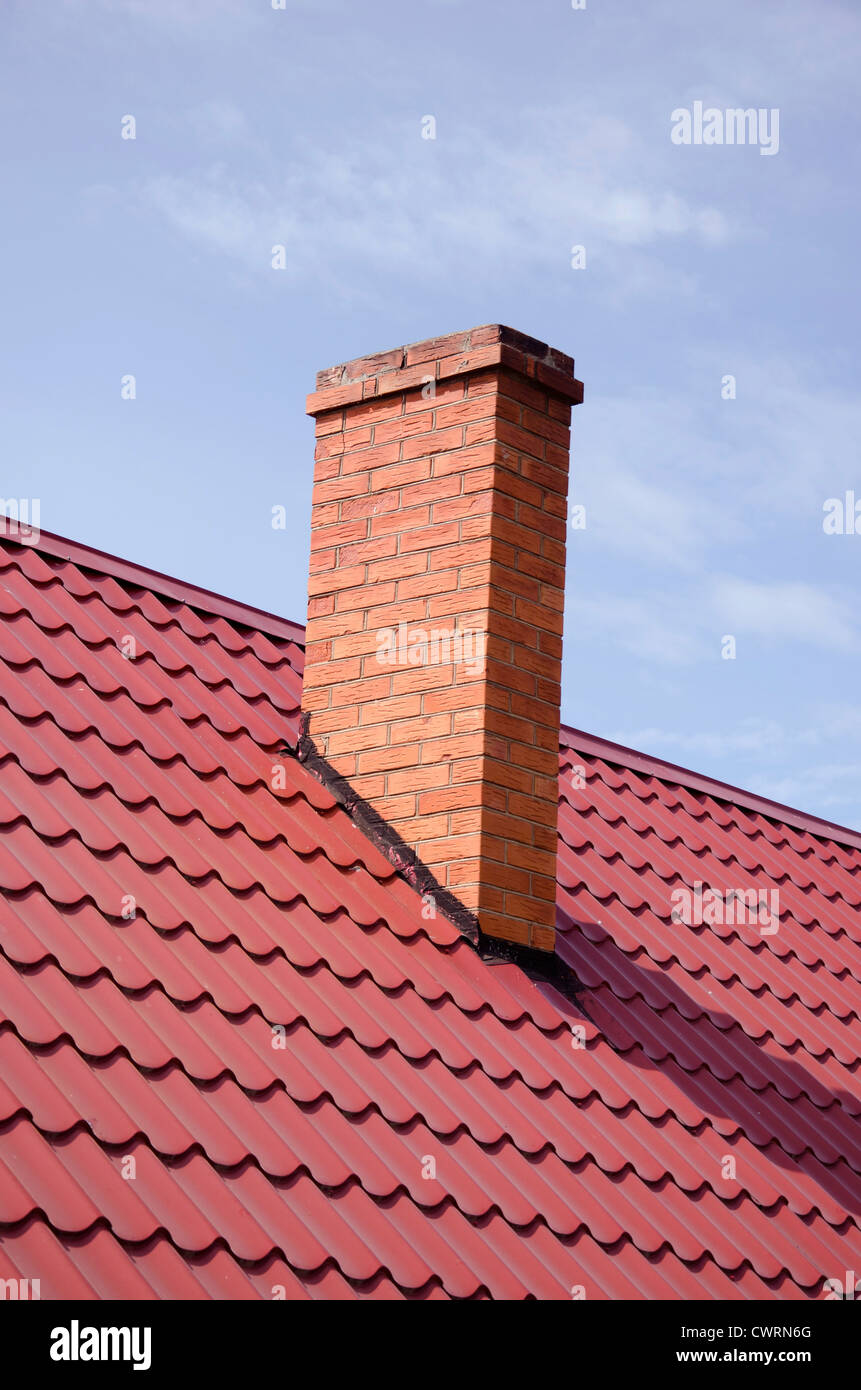 Brown tiled roof and yellow brick chimney on background of cloudy sky. Stock Photo