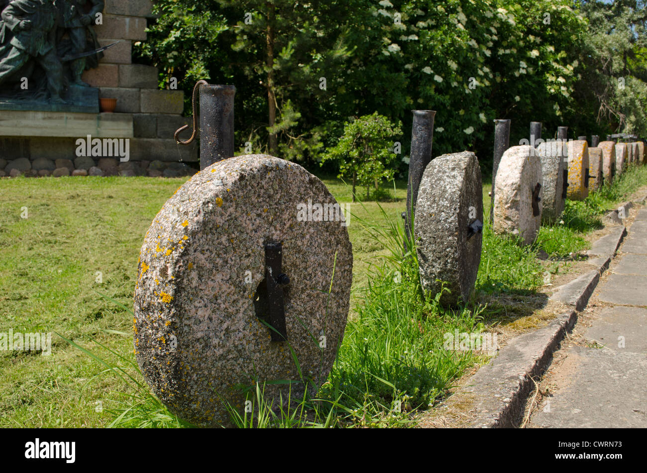 Retro rock millstones hanging on metal columns. Car parking decorations in park. Stock Photo