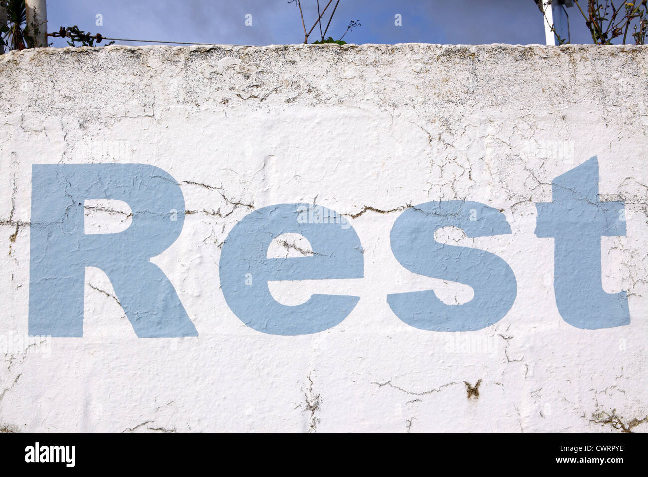 Lettering 'Rest', stencil style sky blue paint on a white washed wall background, crumbling and distressed look, Cornwall, UK Stock Photo