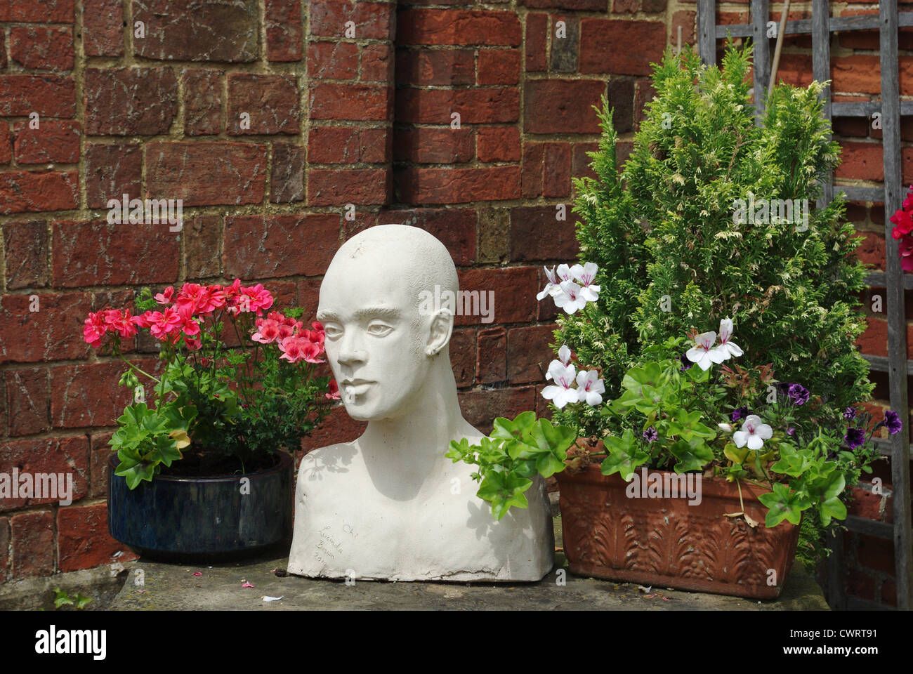 White plaster bust of a man's head, surrounded by flowers and plants Stock Photo