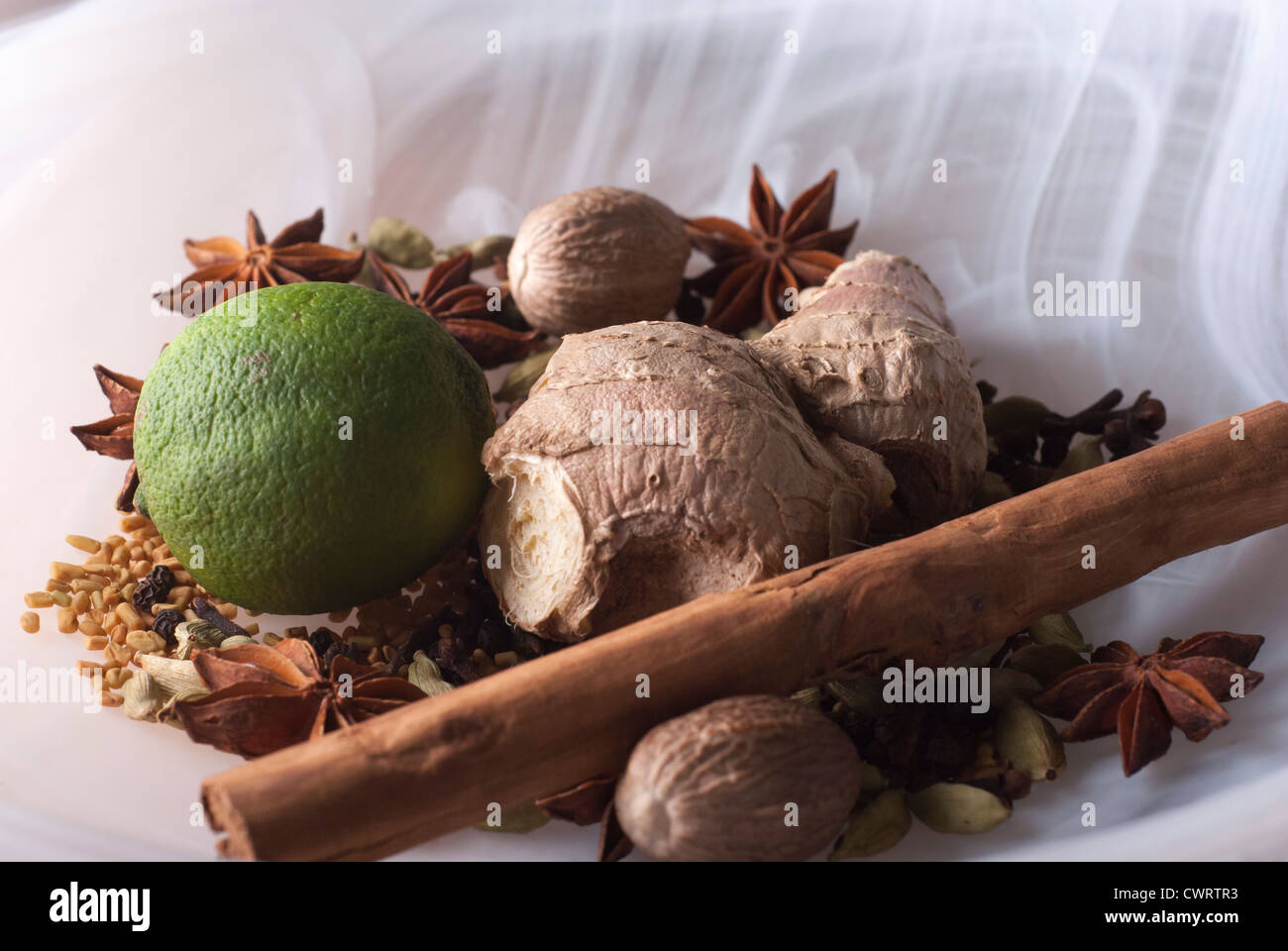 closeup of Ayurvedic ingredients, a lime with whole spices in smoky white glass bowl Stock Photo
