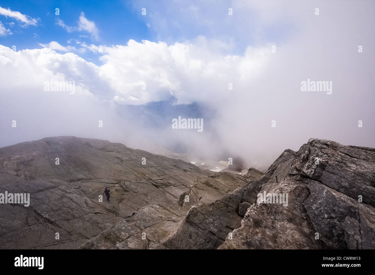 A hiker descends a large slab of rock while on route to Monte Moro Pass on the borders of Switzerland and Italy. Stock Photo