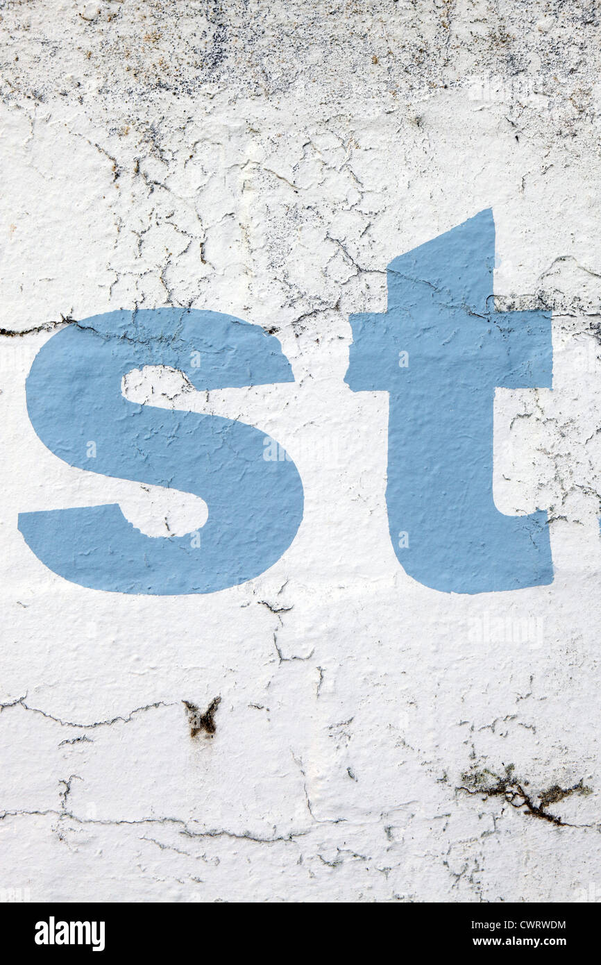 Lettering 'st', stencil style sky blue paint on a white washed wall background, crumbling and distressed look, Cornwall, UK Stock Photo