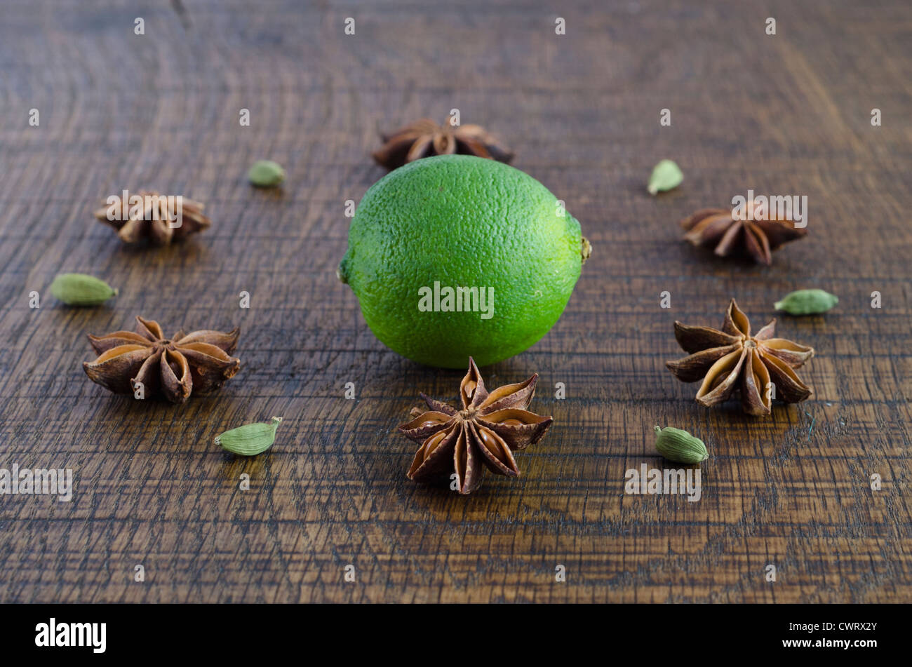 A geometric flower pattern of star anise and cardamom pods around a lime, on a dark wood surface. Stock Photo
