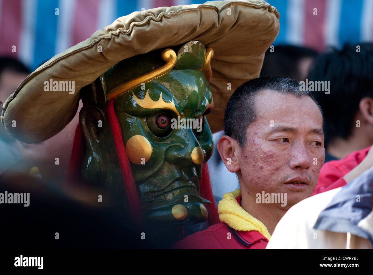 A man stands next to a wooden mask of a god at the 'Pigs of God' festival in Sanxia near Taipei, Taiwan. Stock Photo