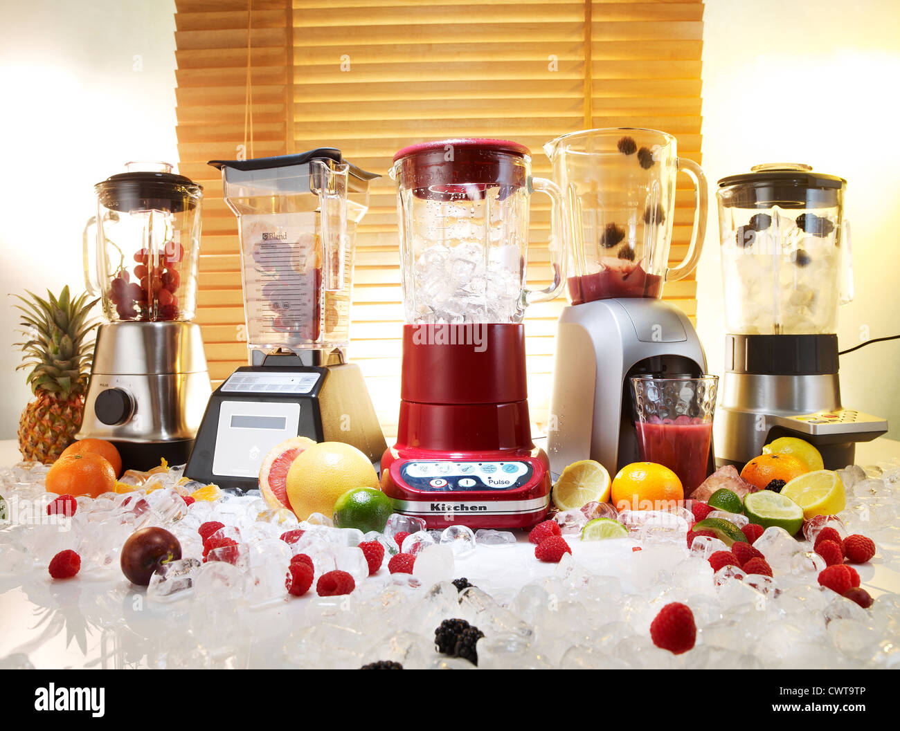 Five blenders and smoothie makers in a kitchen on a bed of ice and fruit Stock Photo