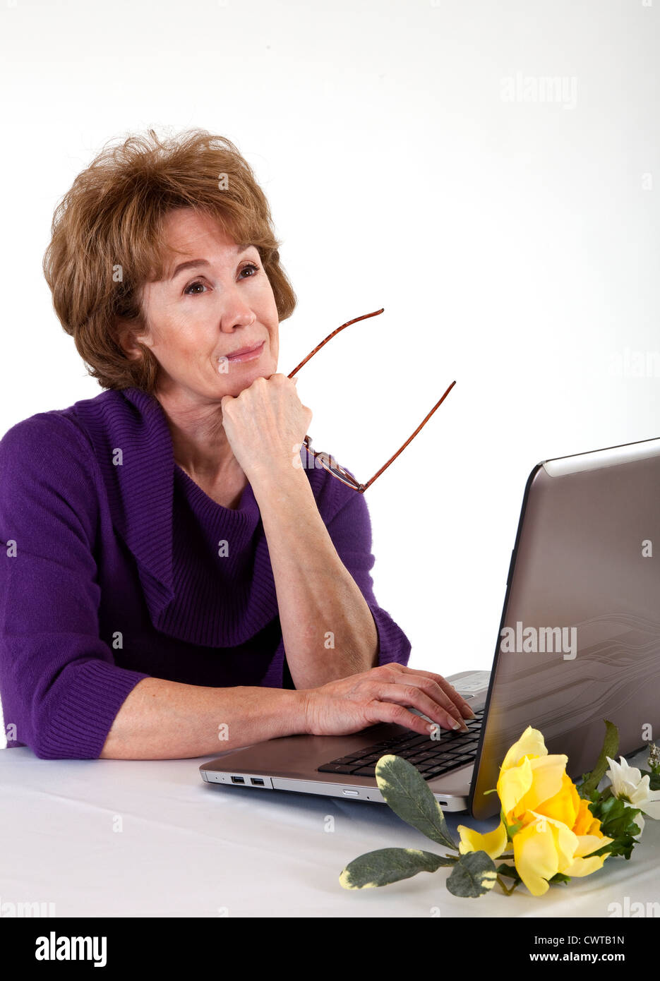 A mature woman sitting in front of her laptop computer with a dreamy sort of expression on her face. Stock Photo