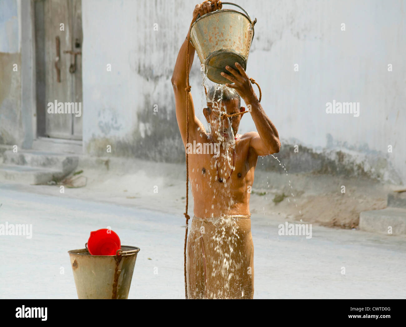 A MAN SPLASHES COOL WATER FROM A WELL, WITH AN AIR TEMPERATURE  OF 40C IN INDIA Stock Photo