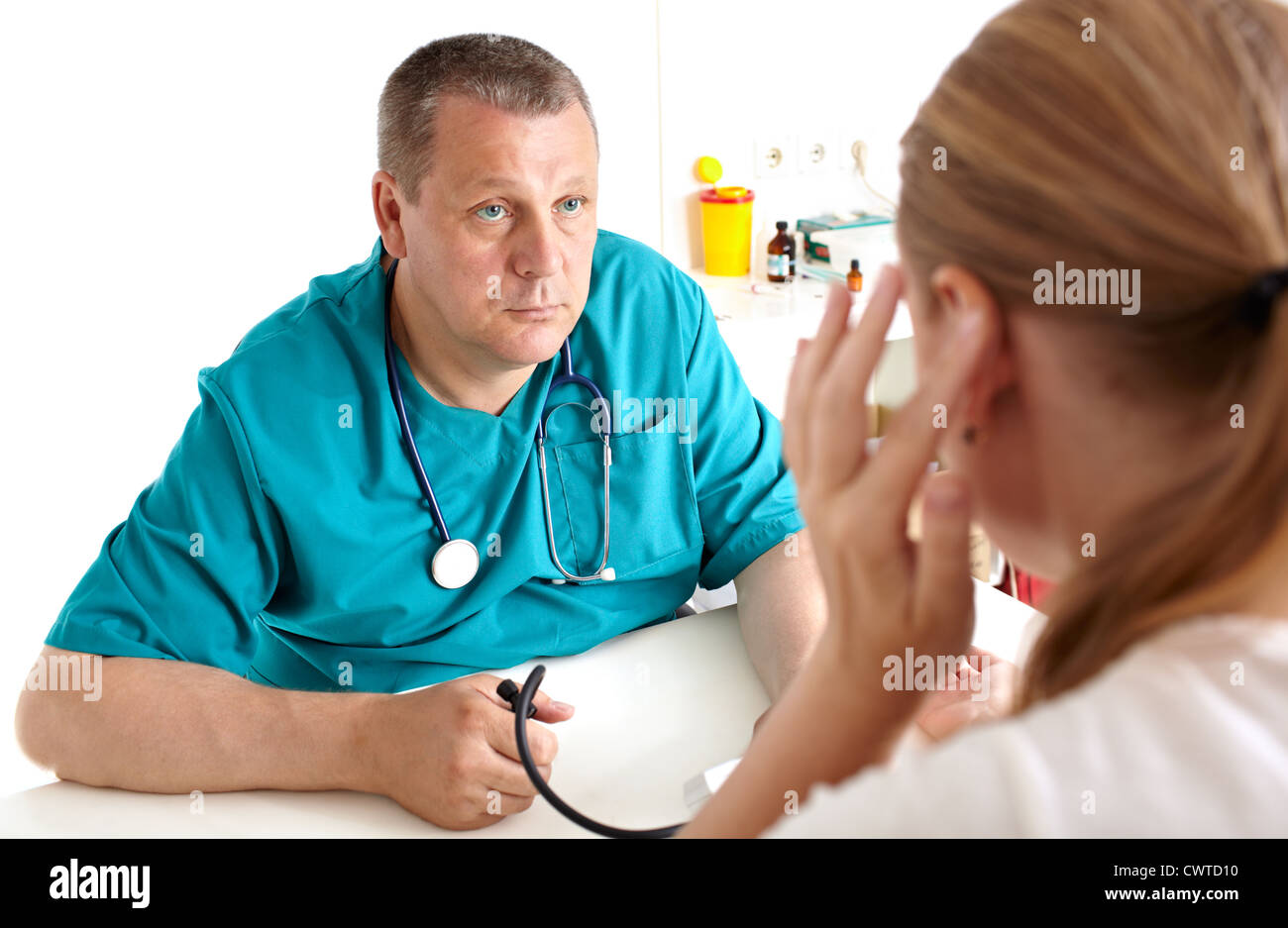A young girl is complaining of headaches. A light medical study. The doctor of 45-50 years old in a green smock. Caucasian. Stock Photo