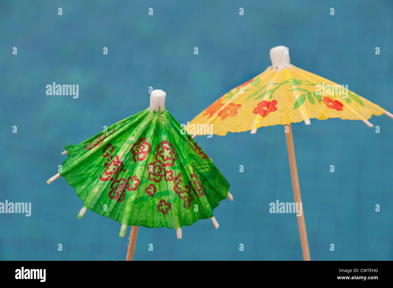 Two colorful paper drink umbrellas are open against a blue background. Stock Photo