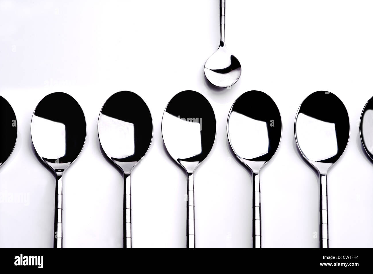 Group of dessert spoons with one teaspoon standing alone. Stock Photo