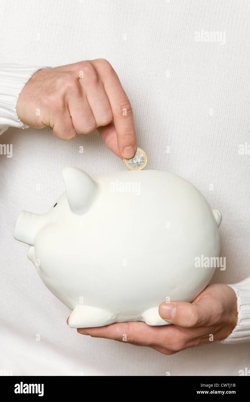 Hand putting Euro coin into piggy bank Stock Photo - Alamy