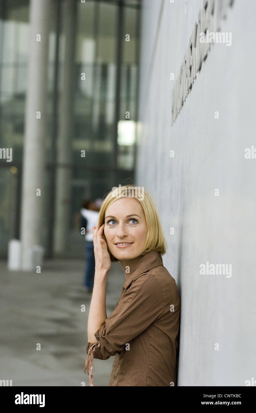 Young woman leaning against concrete wall Stock Photo - Alamy