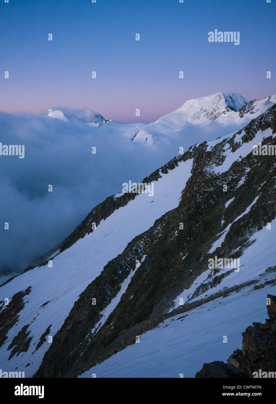 The snow capped summit of Alphubel against the pink and blue dawn sky over Saas Fee in the Alps. Stock Photo