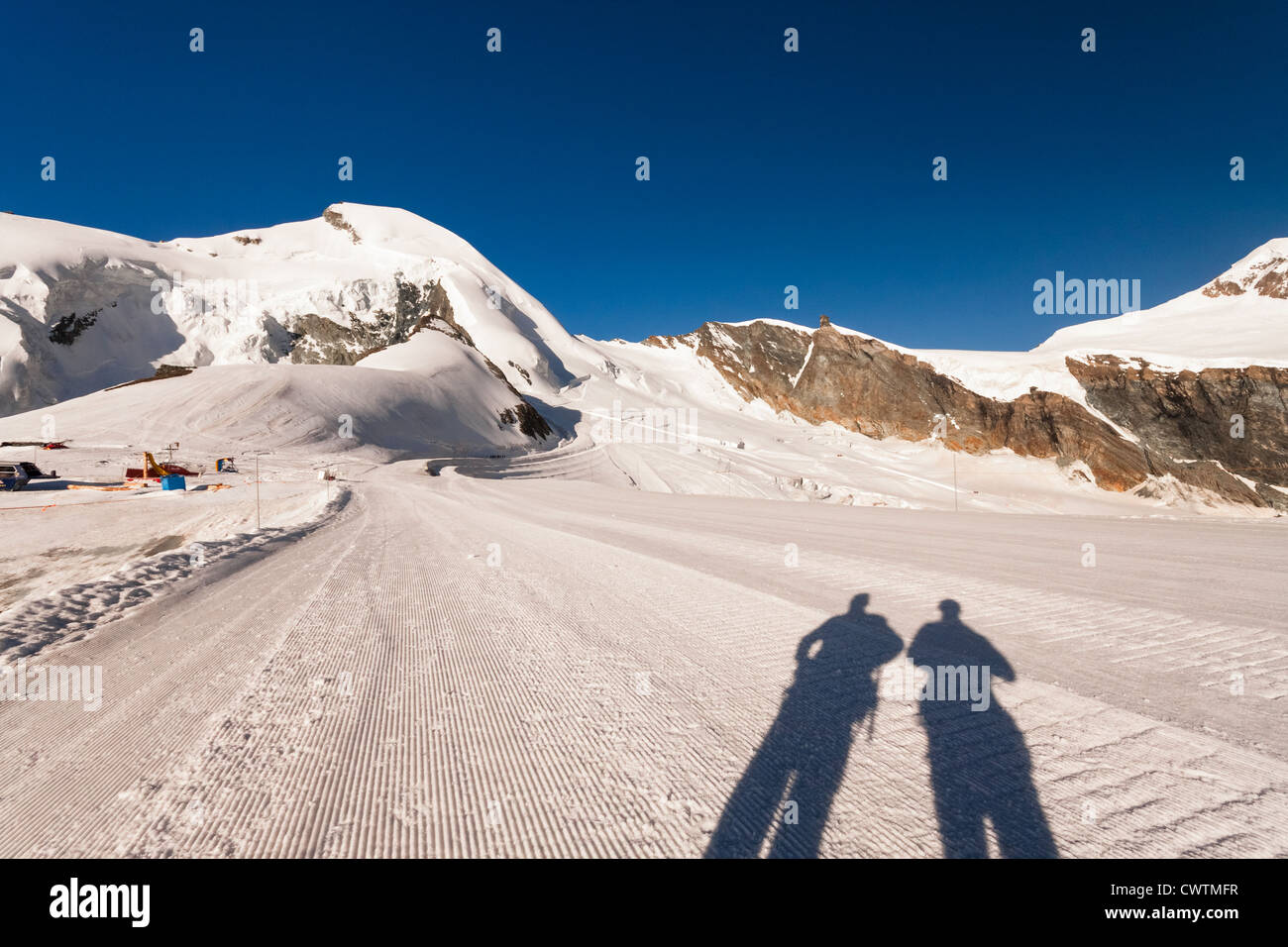 The shadows of two mountaineers on the Piste of Mittel Allalin in Saas Fee Switzerland with Allalinhorn in the distance. Stock Photo