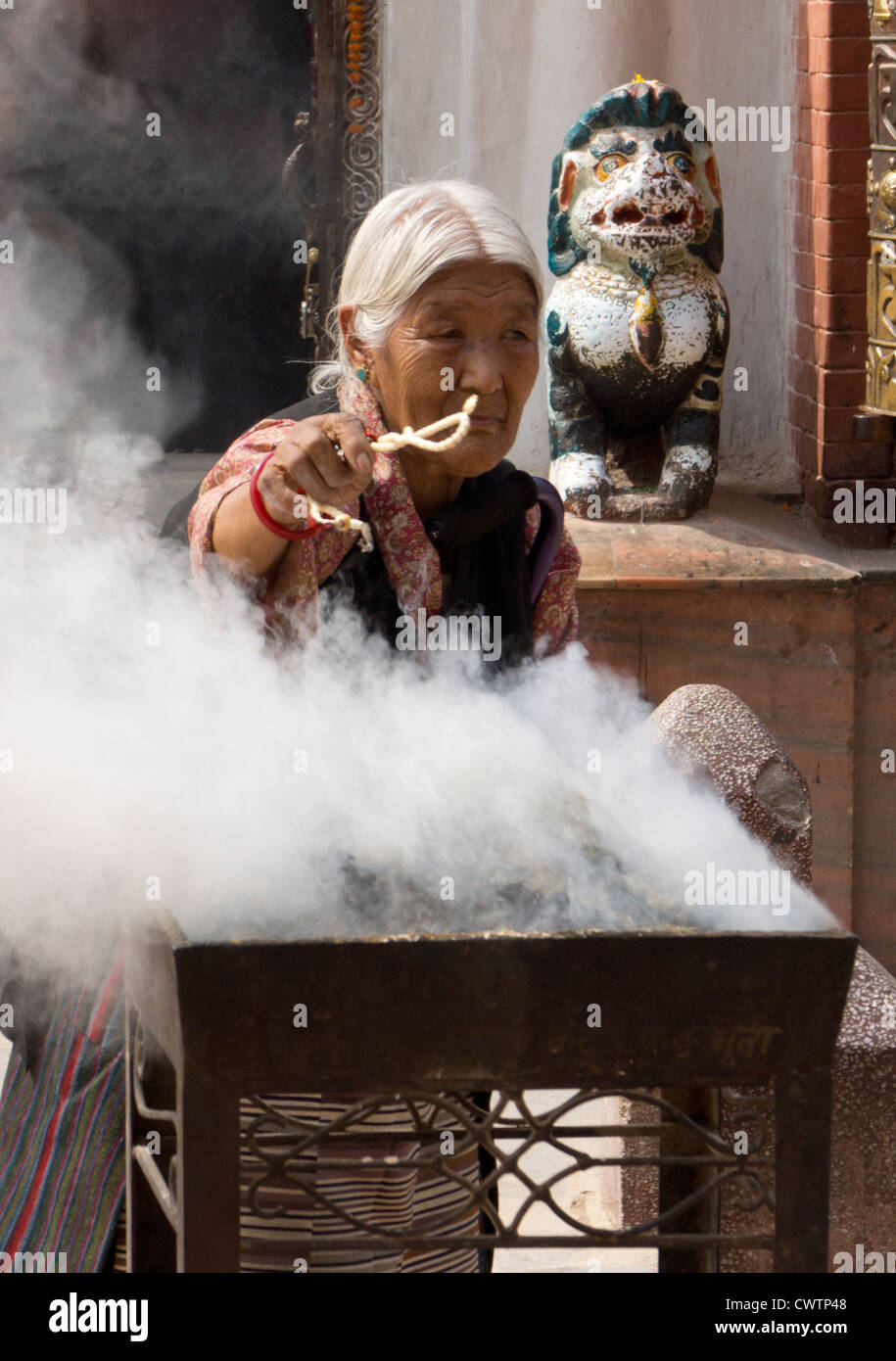 Worshipper purifies her necklace in the smoke at the Boudhanath in Nepal Stock Photo