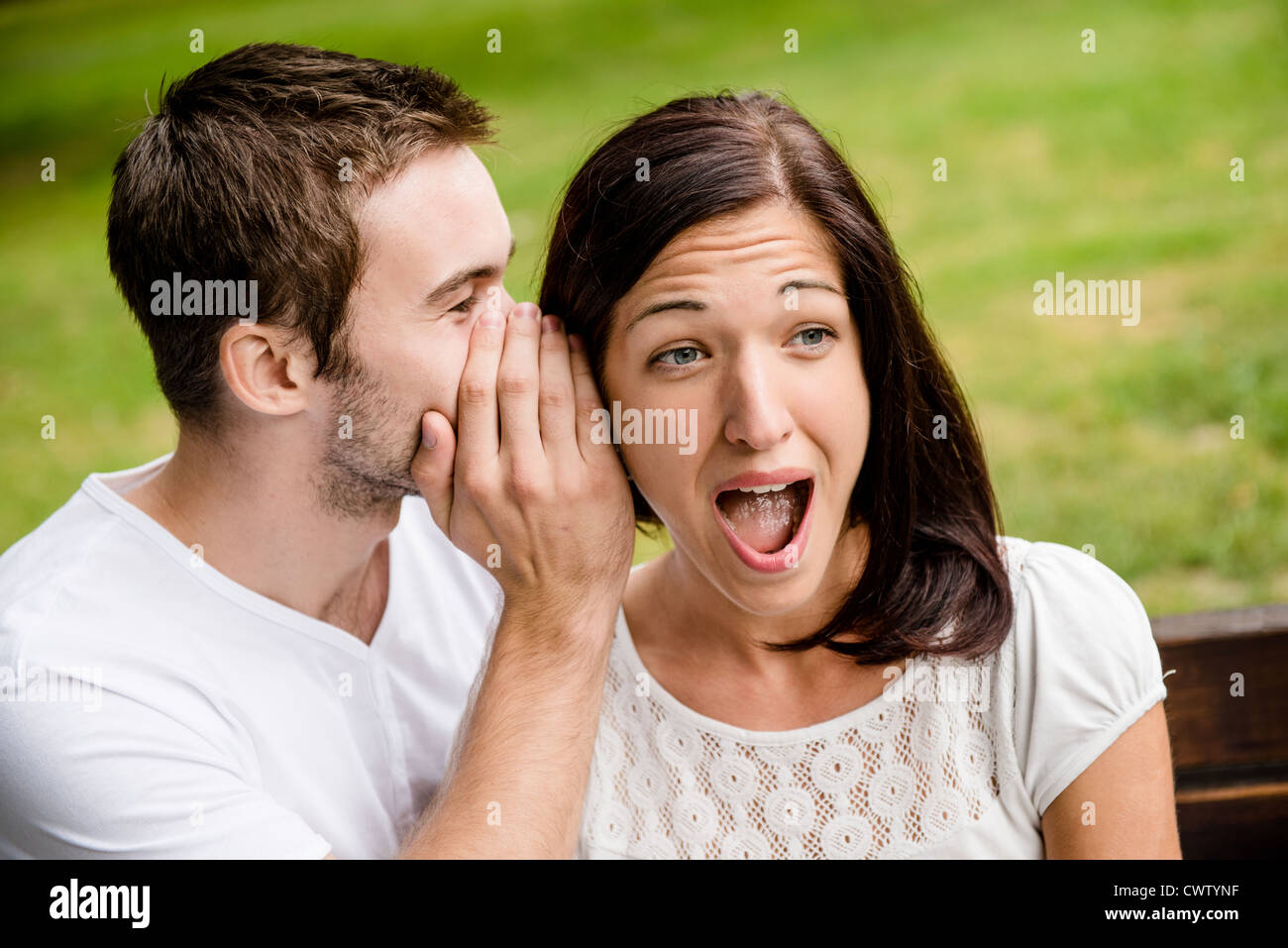 Young man whispering to woman (girlfriend) - surprise expression Stock Photo