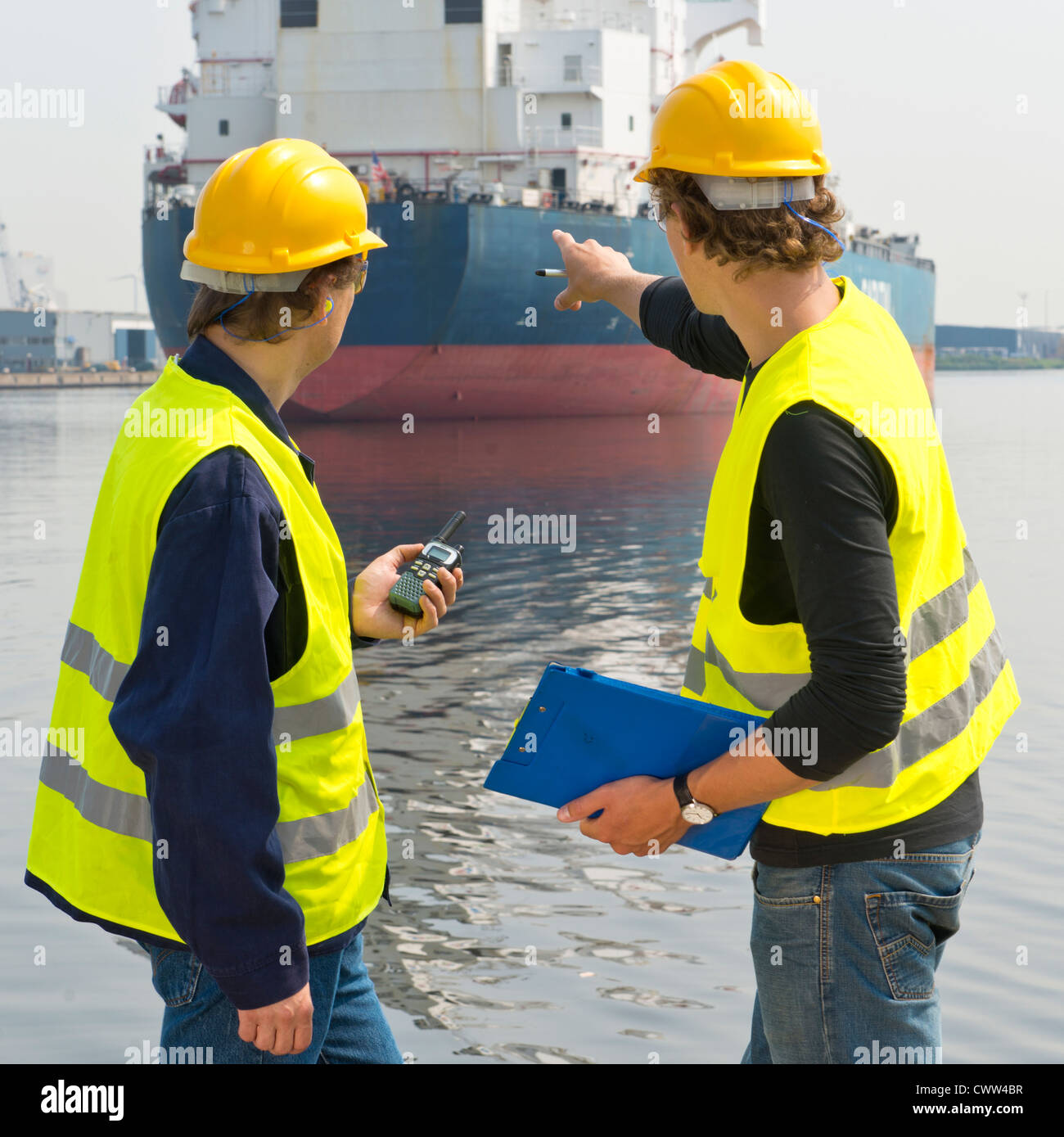 Two dockers discussing an issue with a moored ship in an industrial radio with the ships log and a cb radio at hand Stock Photo