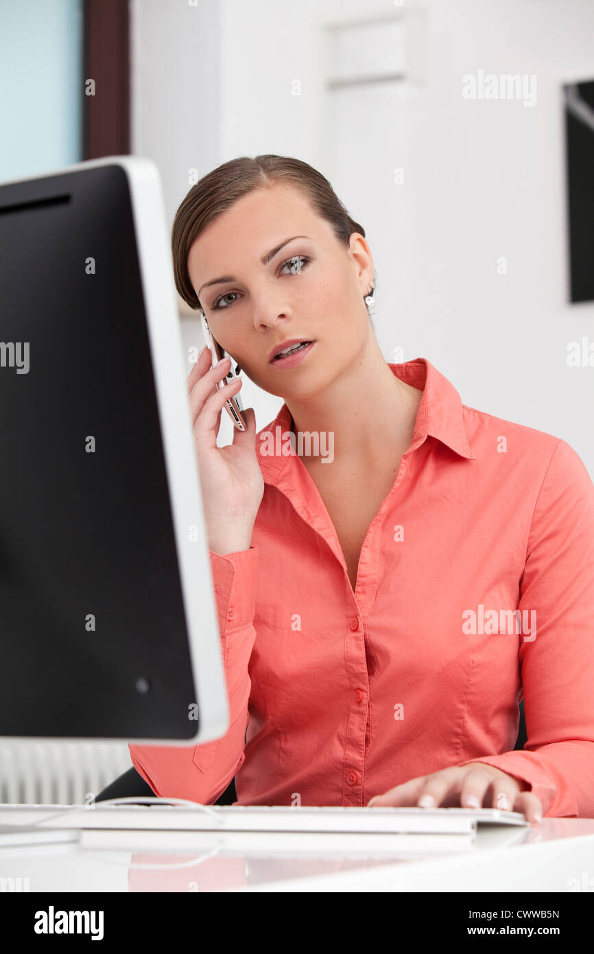 Young brunette businesswoman at desk with cell phone and computer Stock Photo