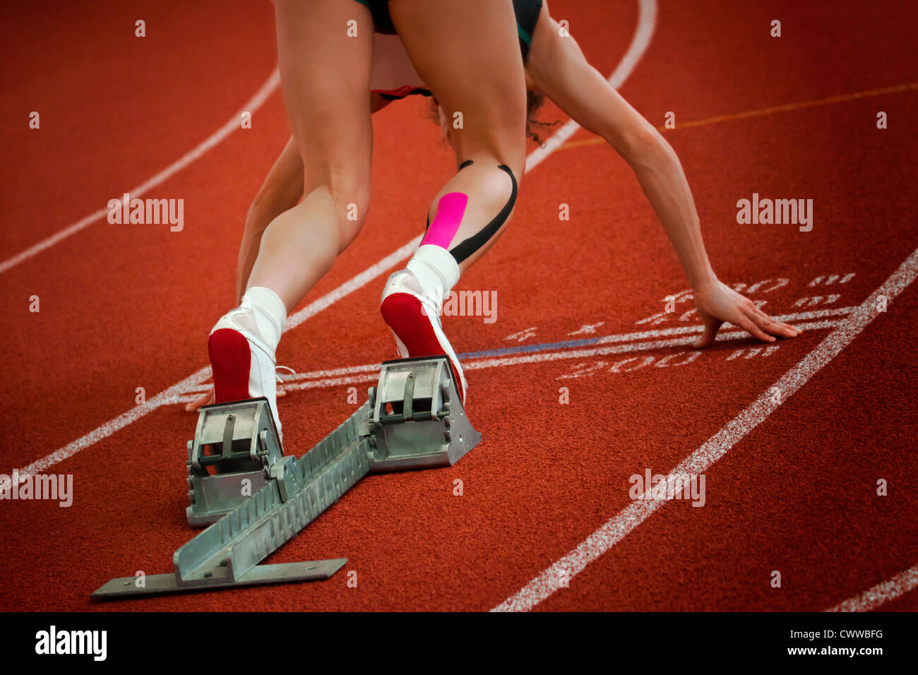 Female short distance runner on gravity slope curve is in start position Stock Photo