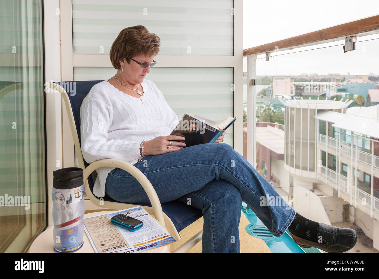 Woman reading book while sitting on cruise ship balcony at harbor in Tampa, Florida Stock Photo