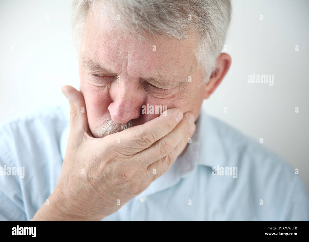 senior man holds his hand to his mouth while feeling nauseous Stock Photo