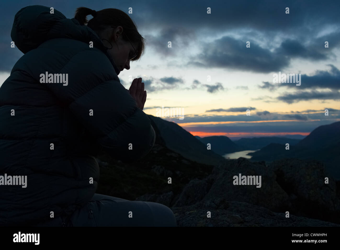 A woman praying to God on the summit of a mountain. Stock Photo