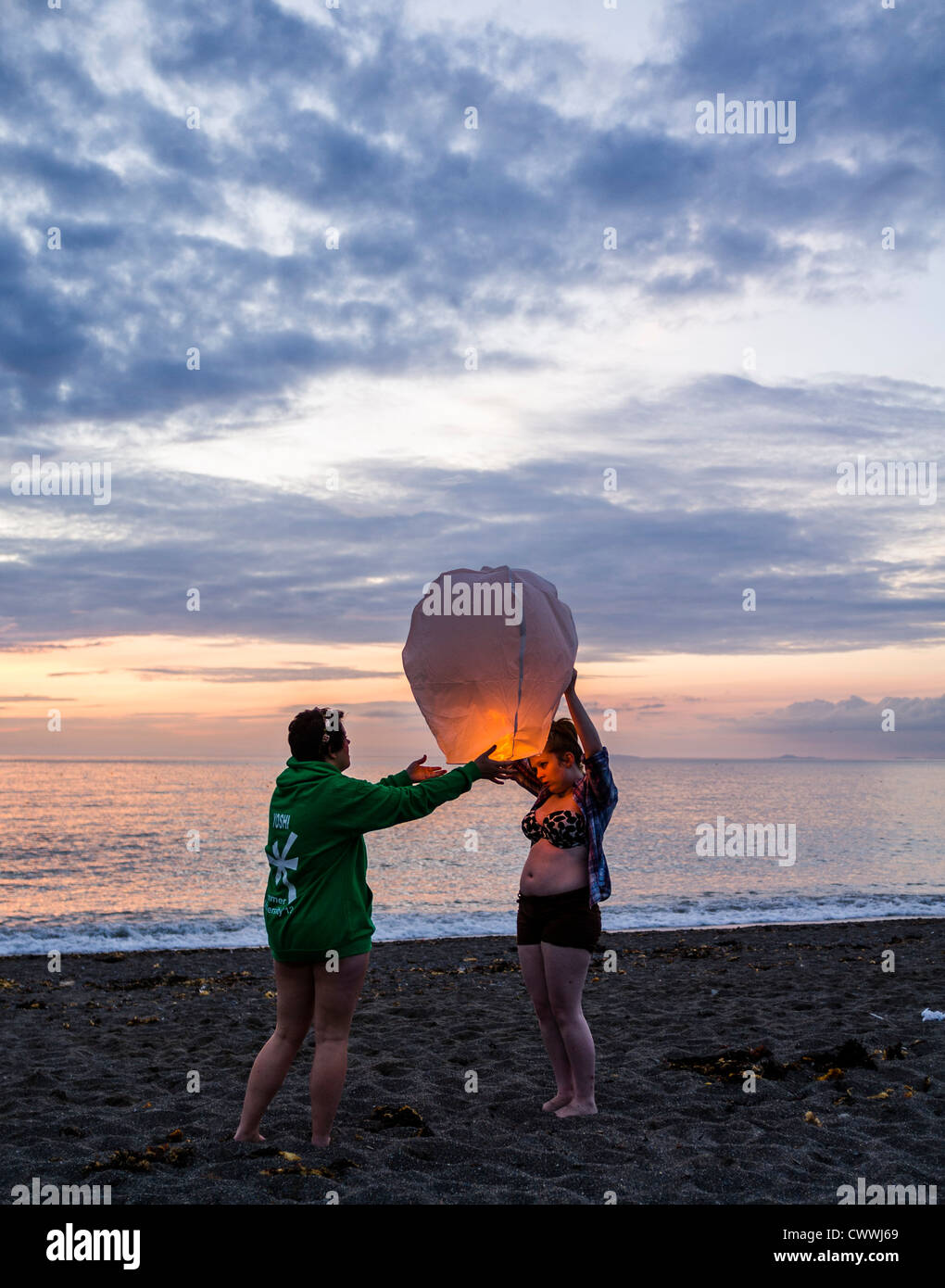 Summer evening : A young couple setting off a chinese paper lantern on the beach at dusk Aberystwyth Wales Uk Stock Photo