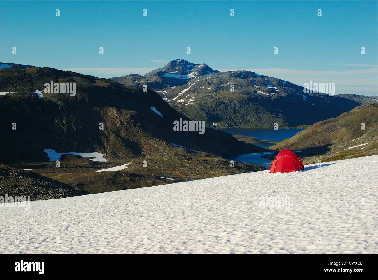 Camping with a red tent on a snowfield with a view on mountains and lakes along the Nordkalottleden, Scandinavia Stock Photo