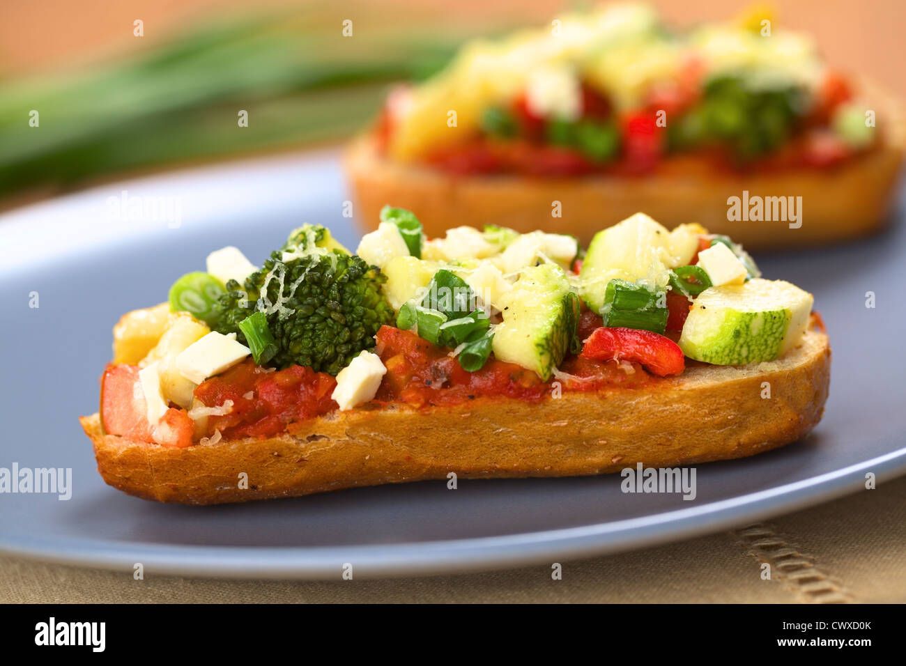 Baked vegetarian open sandwich (red bell pepper, broccoli, zucchini, scallion and cheese on spicy tomato sauce on a bun) Stock Photo