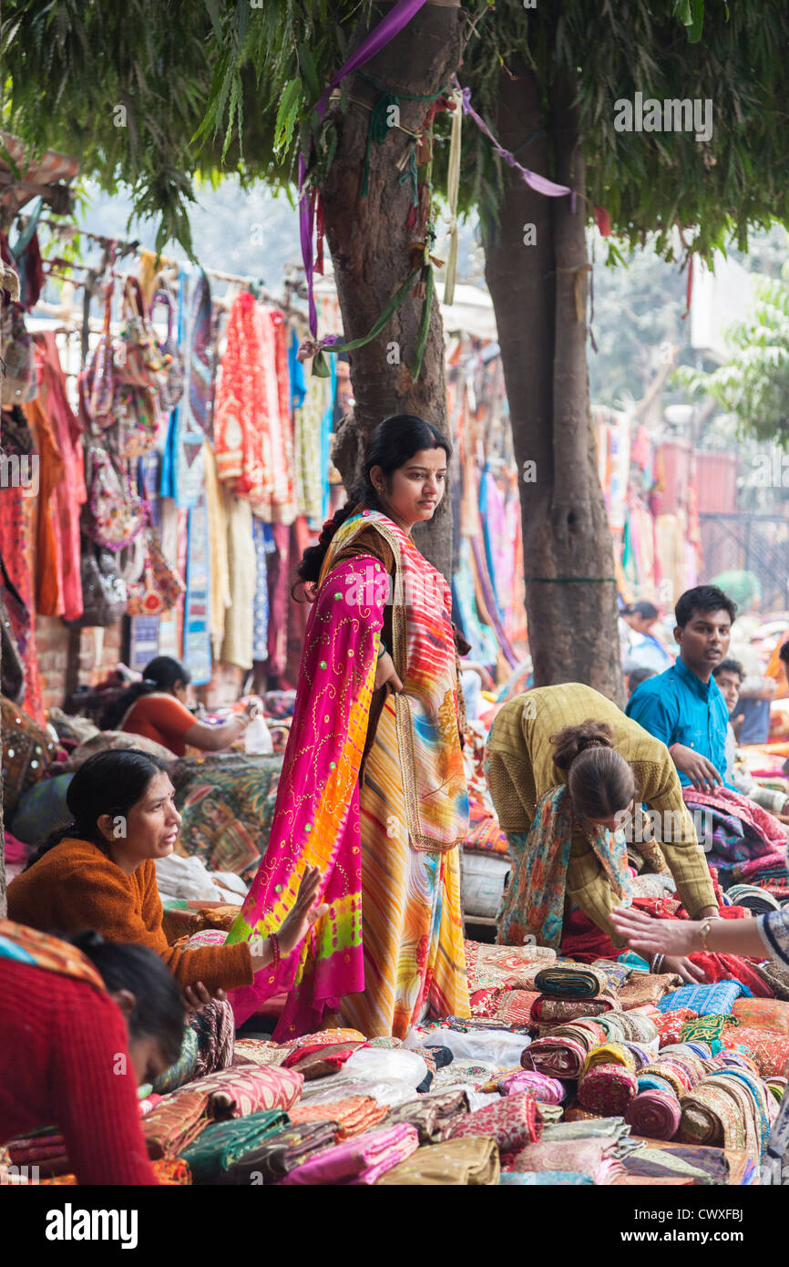 New Delhi roadside street market, sellers selling carpets, cloth and clothes, one woman in brightly coloured traditional sari Stock Photo