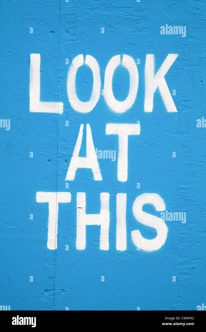 White stencilled graffiti on a blue painted wall with the words: Look At This Stock Photo