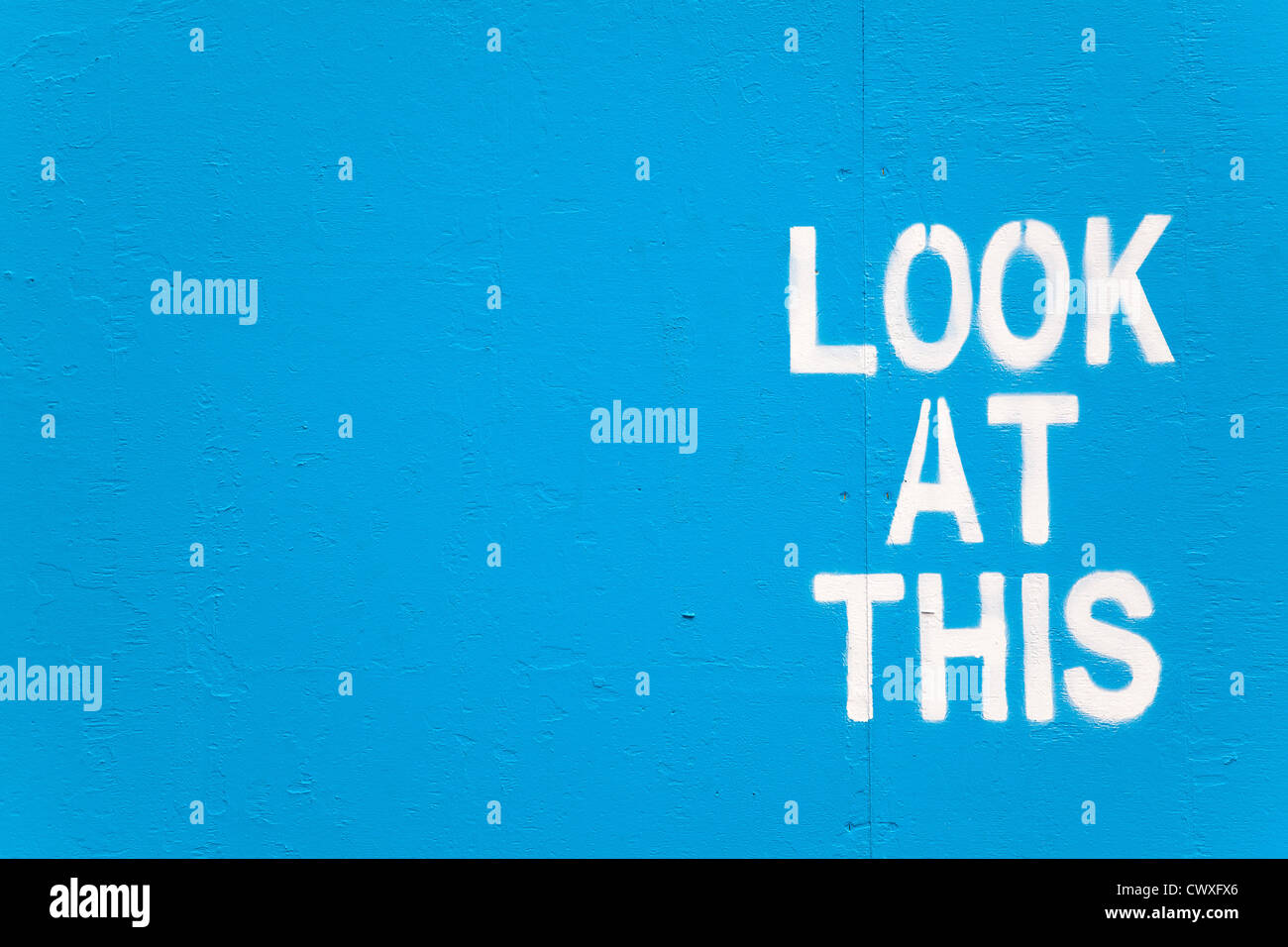 White stencilled graffiti on a blue painted wall with the words: Look At This Stock Photo
