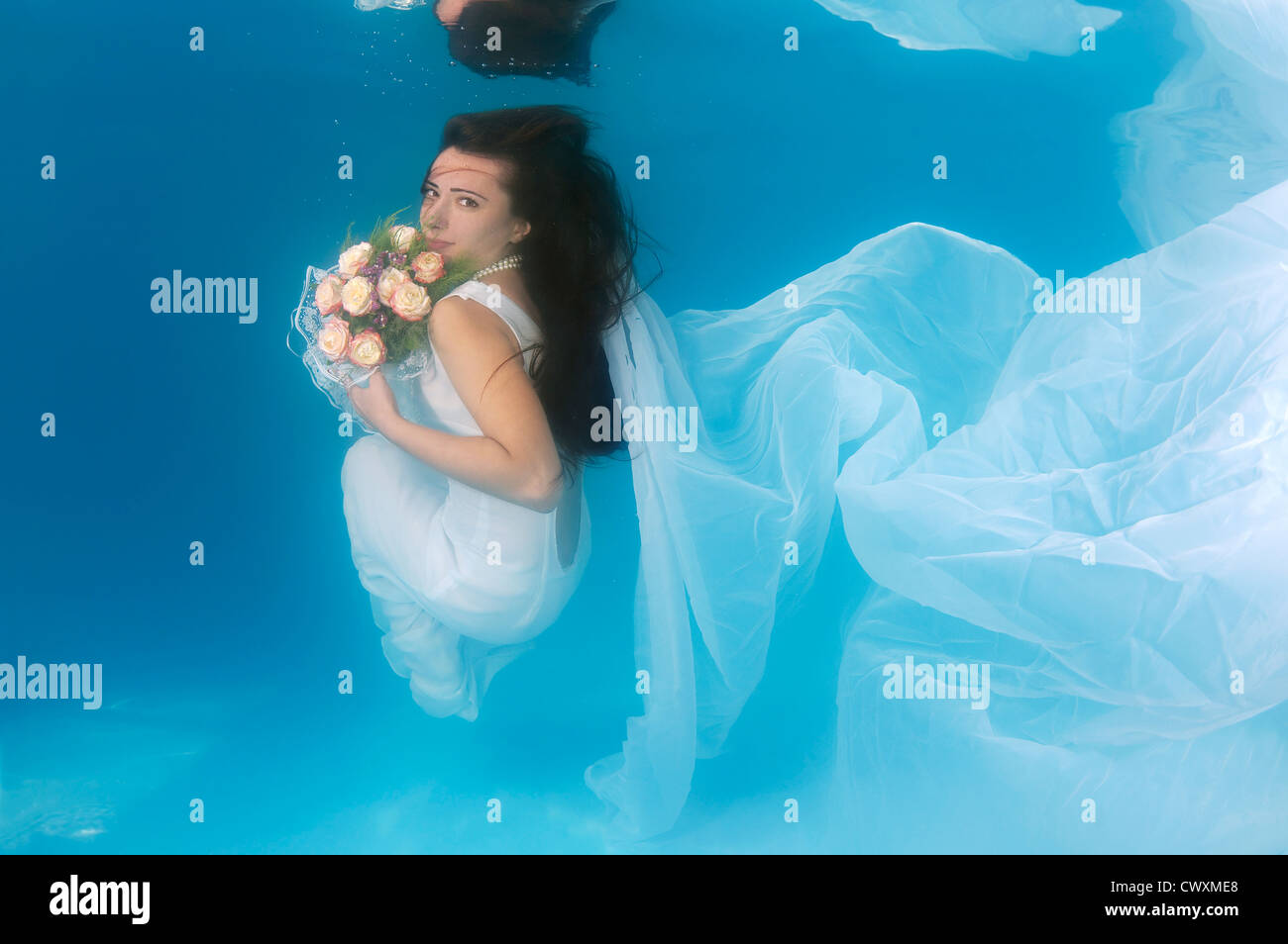 A young woman with big hair posing in a pool underwater Stock Photo