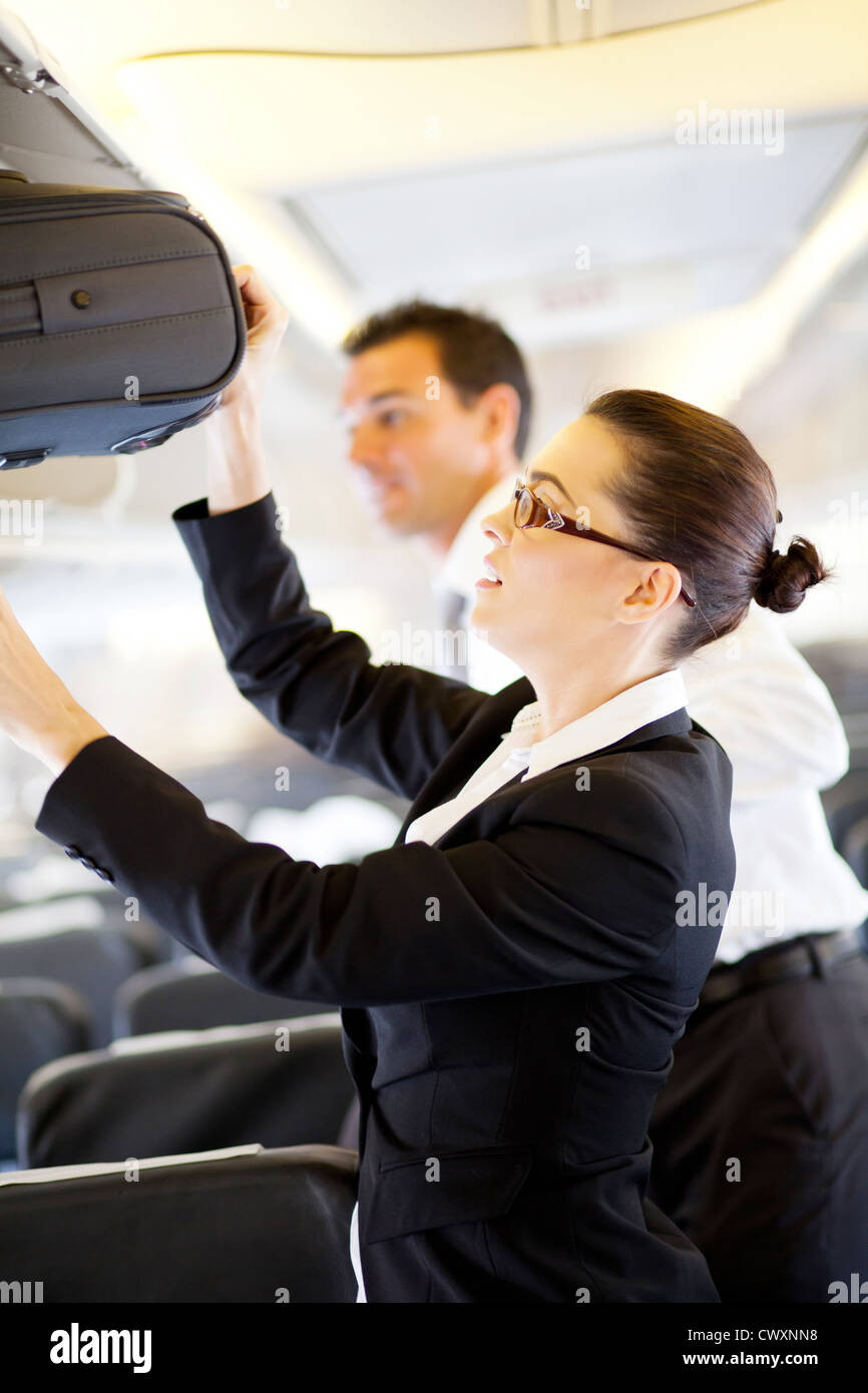 friendly flight attendant helping passenger with carry on luggage Stock Photo
