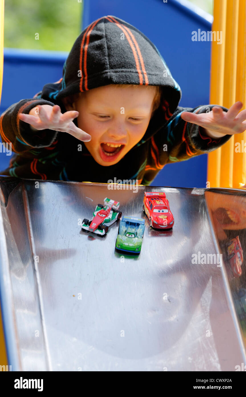 A young boy playing with toy cars on a slide Stock Photo
