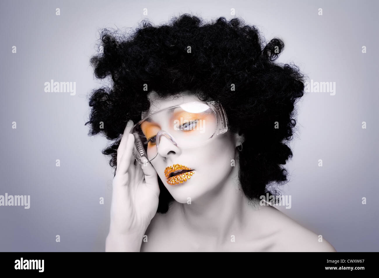 Young caucasian woman with gold fashion makeup and gold diamonties on her lips wearing a black afro wig Stock Photo