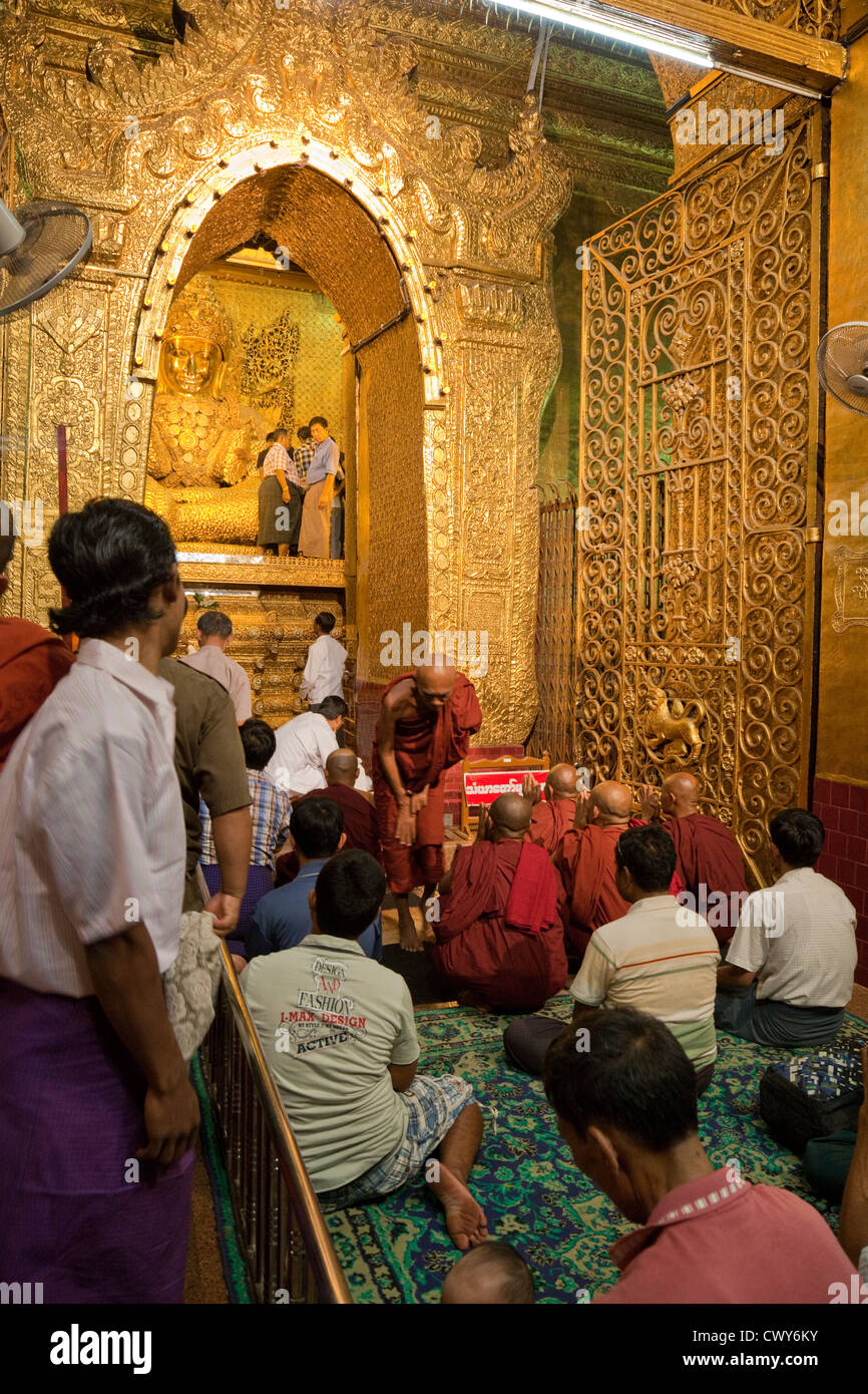 Myanmar, Burma. Mandalay. Mahamuni Buddhist Temple. Worshipers sit in veneration of the Buddha, covered in gold leaf. Stock Photo