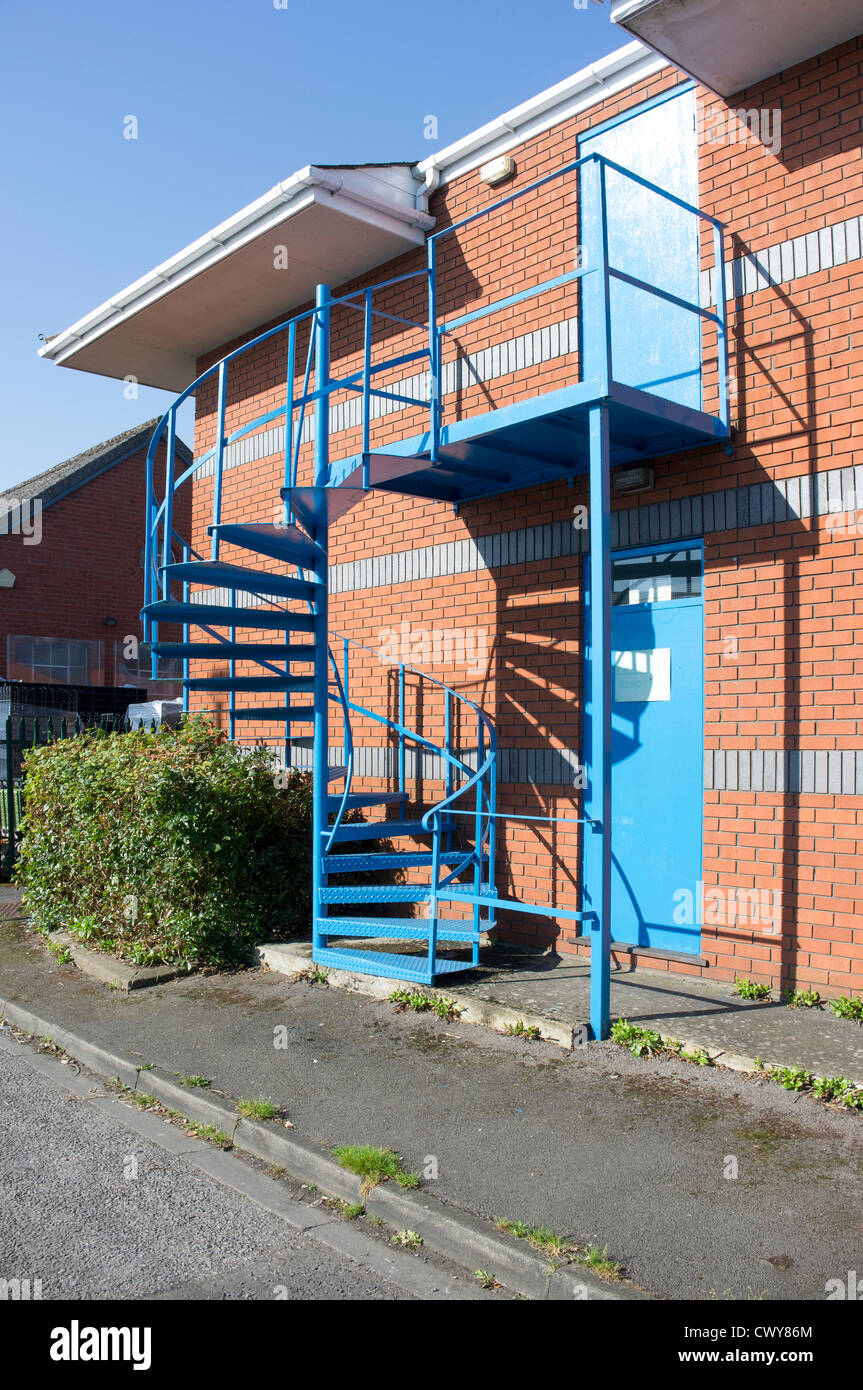 Blue painted steel spiral staircase fire escape on side of industrial building Stock Photo