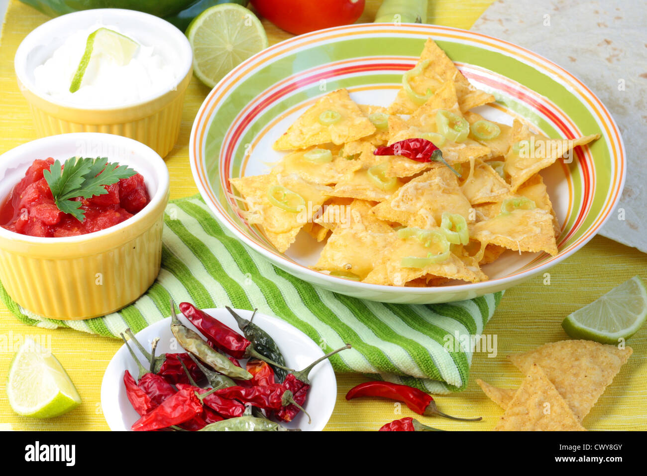 Nachos covered in melted cheese and jalapeno peppers. With dishes of