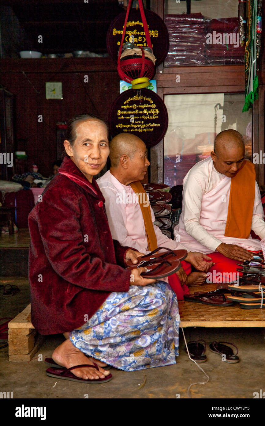 Myanmar, Burma. Mandalay. Two Buddhist Nuns and Friend Examining Sandals. Buddhist nuns shave their heads, as do men. Stock Photo
