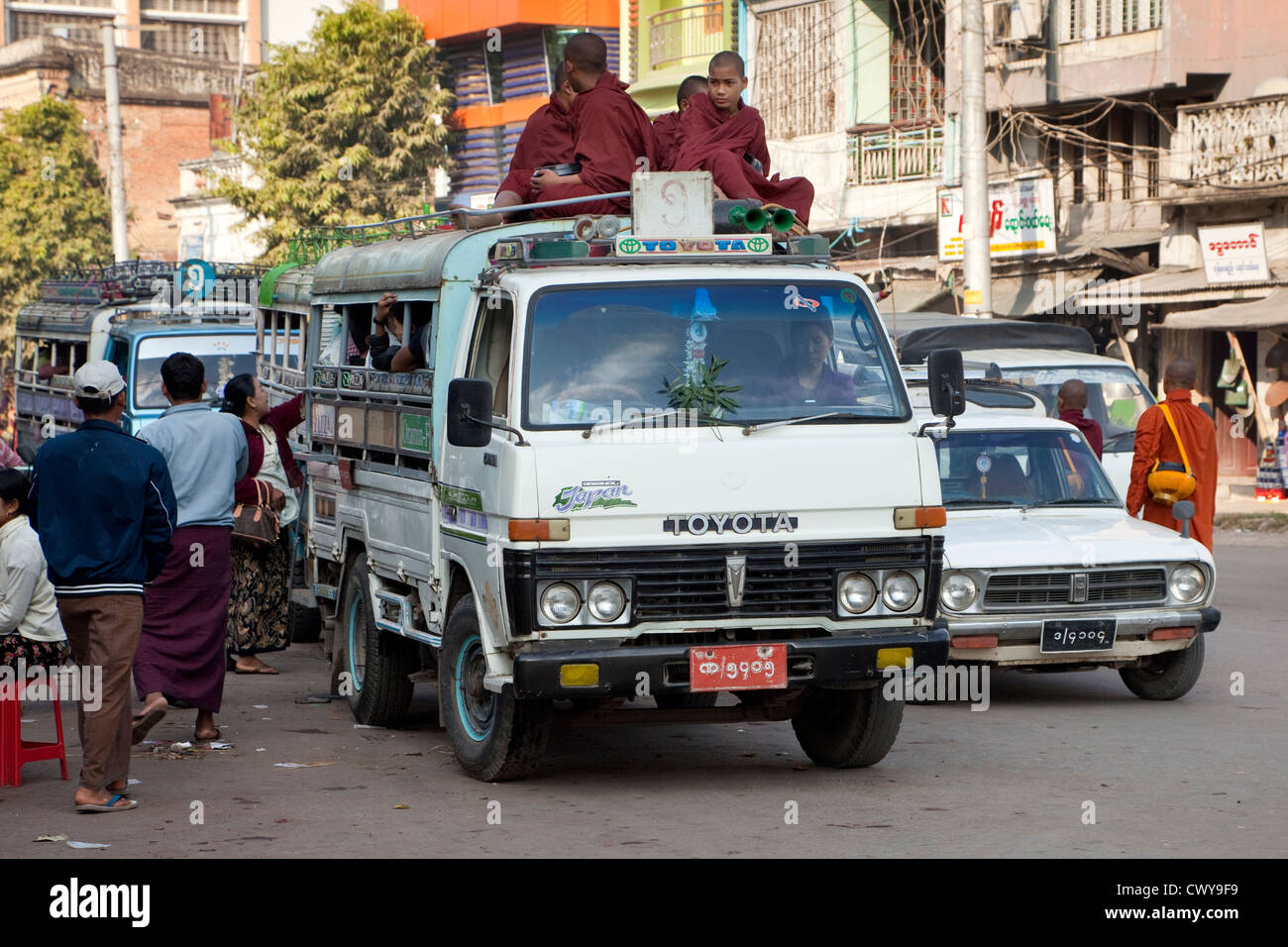 Myanmar, Burma, Mandalay. Novice Monks Riding on top of a Van in downtown Mandalay Traffic. Stock Photo