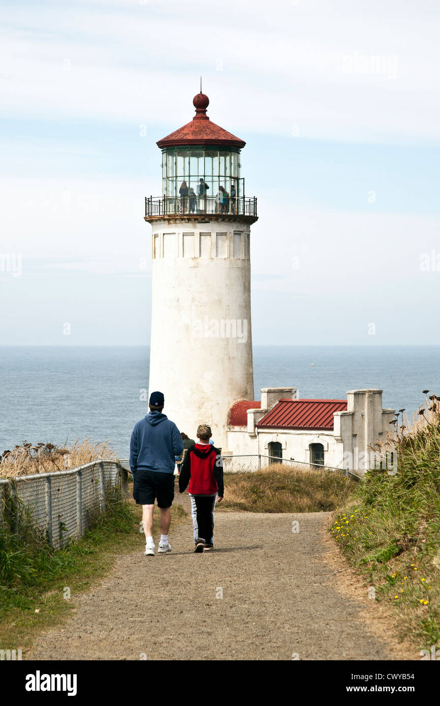 dad & young son walking on path leading to 1898 North Head Lighthouse where group is visible touring lantern room Ilwaco Stock Photo