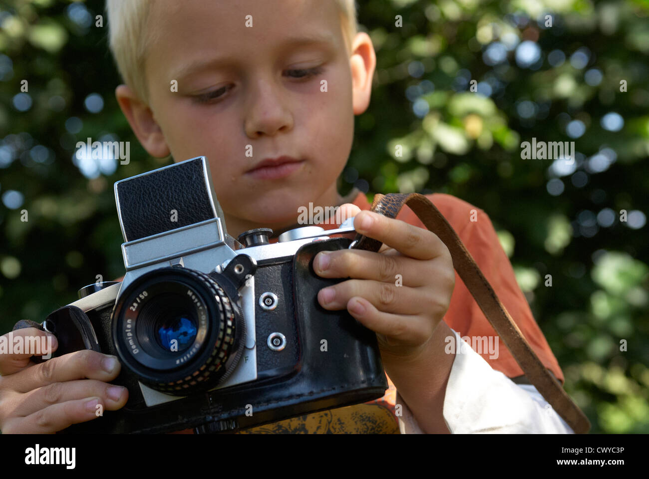 Child blond boy holding and photographing with vintage camera outside summertime Stock Photo