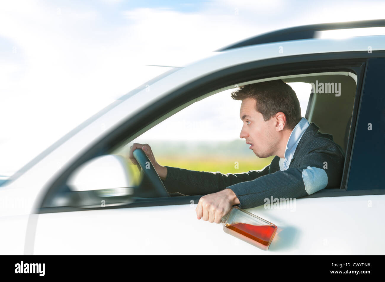 Drunk man holding bottle of whiskey in left hand. Person driving and drinking alcohol. Outdoor action with young guy inside Stock Photo