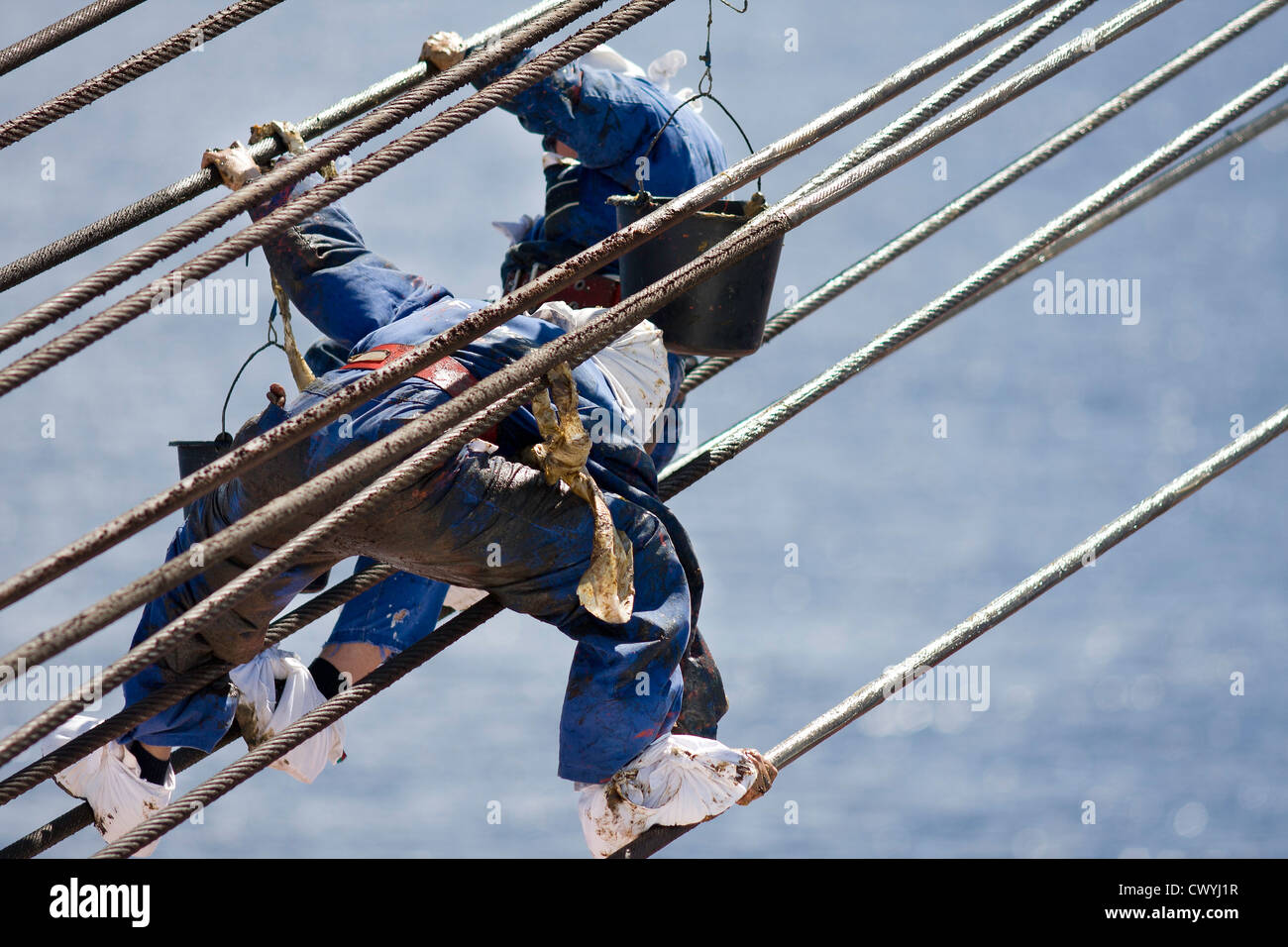 Two seamen during ship's crane maintenance greasing crane's steel wires