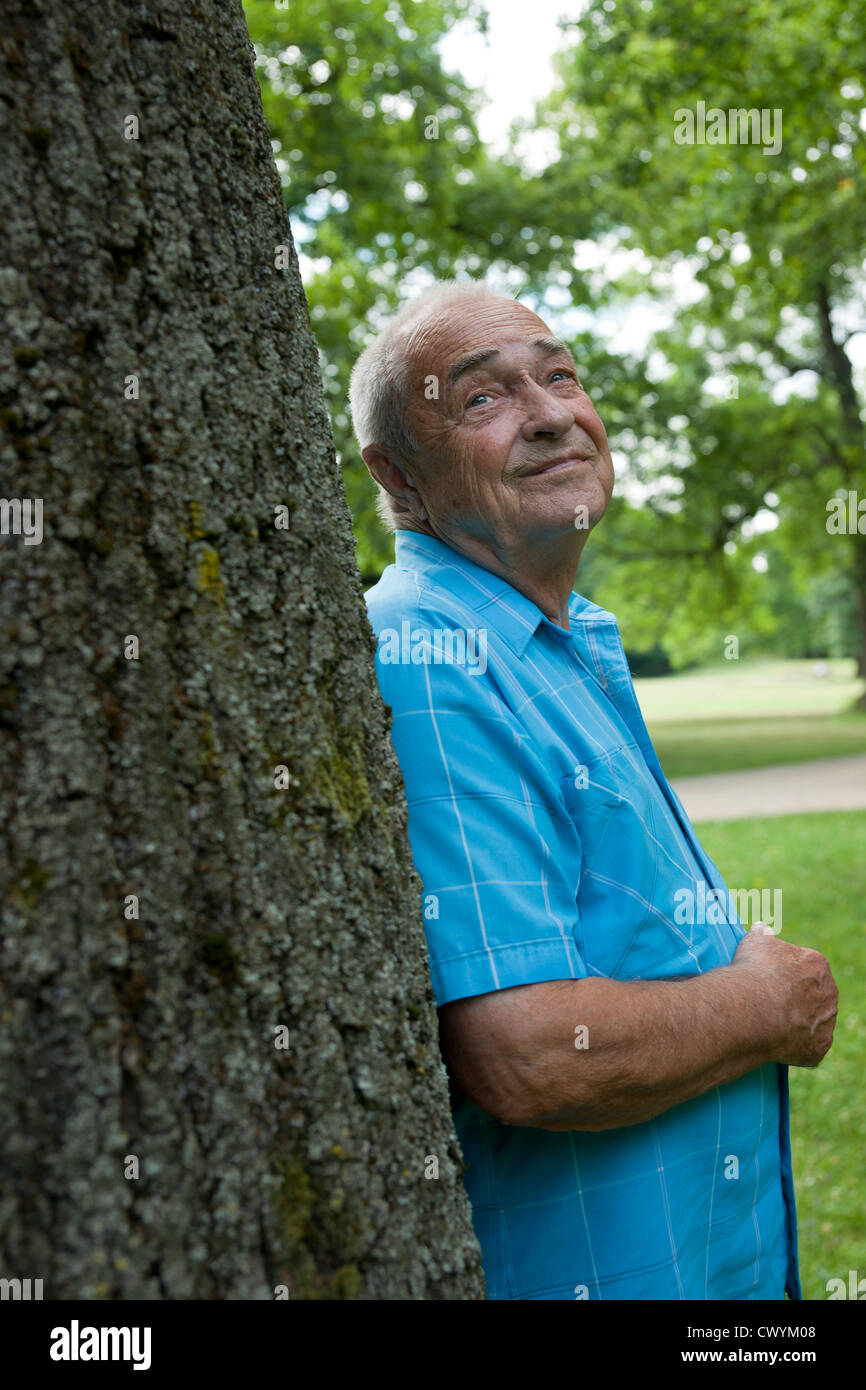 Old man at tree trunk looking up Stock Photo